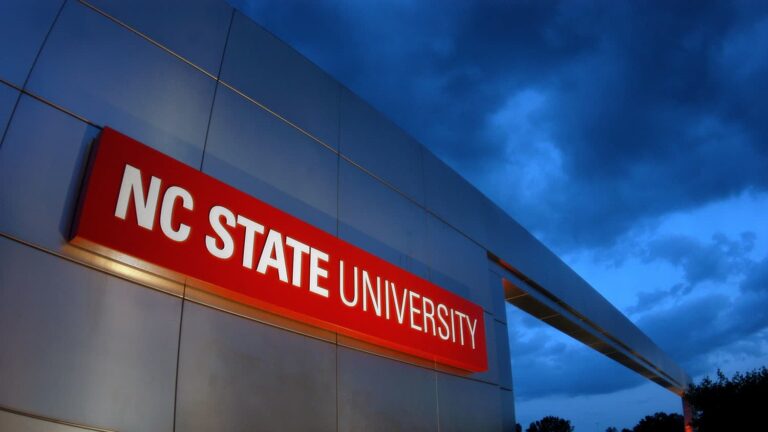 NC State logo on a building with sky and clouds in the background